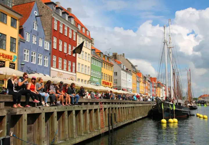 Bunte Häuser am Nyhavn, Kopenhagen an einem Tag. Menschen sitzen am Kai, Boote liegen im Wasser.