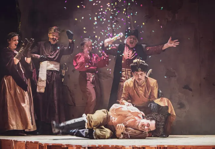 Aktorzy w strojach ludowych świętują na scenie, sypiąc konfetti. To fragment repertuaru teatru ludowego.