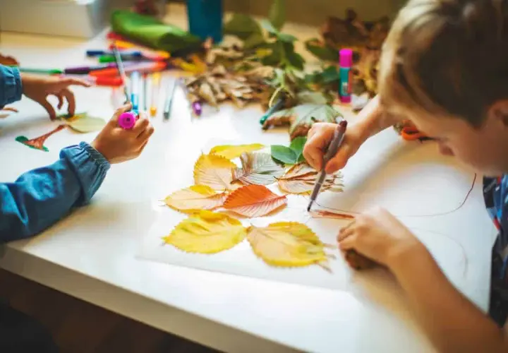 Niños de otoño creando arte con hojas secas y rotuladores.