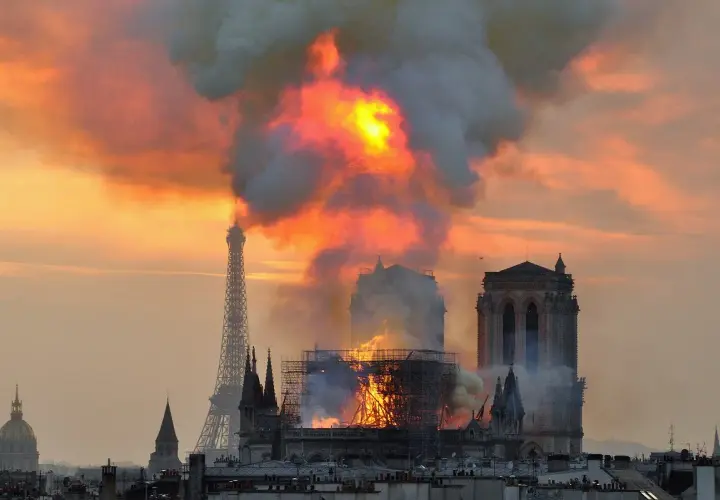 Płonąca katedra Notre-Dame w Paryżu z Wieżą Eiffla w tle.