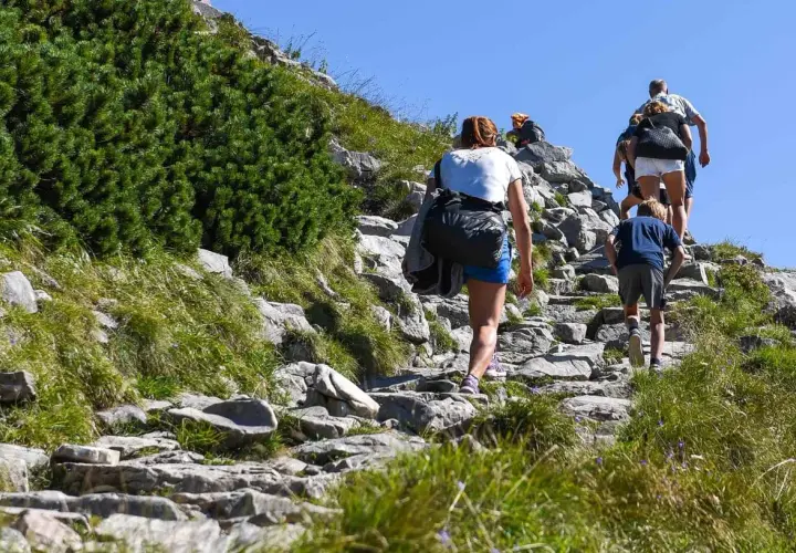 Rodzina wspina się kamienistym szlakiem. Dziecko idzie z przodu, a za nim dorośli. To ich wejście na Giewont.