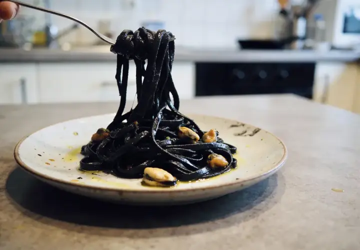 Pâtes noires, colorées avec de l'encre de seiche, c'est quoi ce plat savoureux ? Elles sont servies avec des moules sur une assiette.