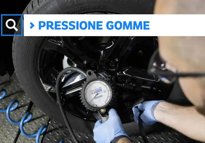 Controllo pneumatici: un uomo con guanti blu usa un manometro per verificare la pressione di una gomma.