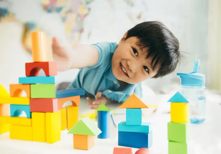 Niño sonriente jugando con bloques de colores, creando torres y casas. Perfectos juegos niños 3 años en casa para la imaginación.