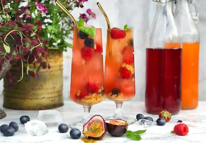 Två glas med fruktiga drinkar, fyllda med bär och passionsfrukt. Perfekt för en somrig bål med bubbel.