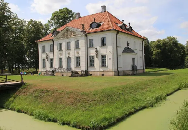 Pałac w Choroszczy otoczony fosą i zielenią, z drewnianym mostkiem prowadzącym do rezydencji.