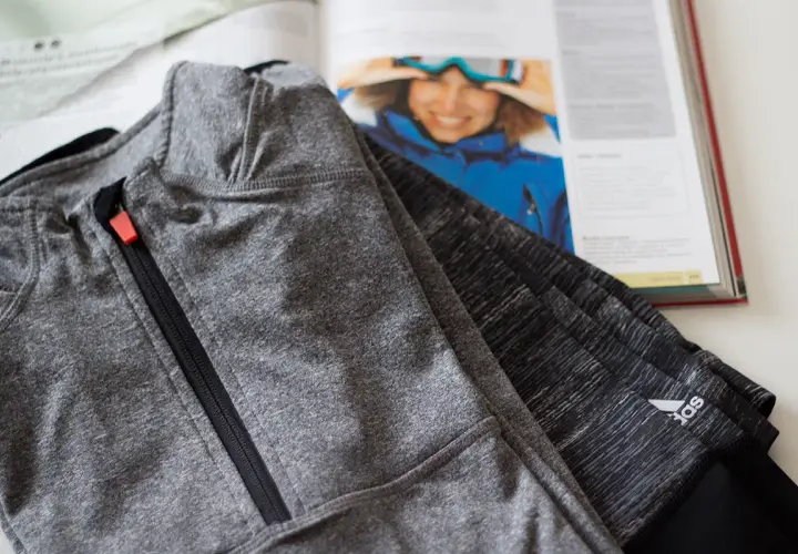 Szara bluza sportowa z zamkiem, wykonana z poliamidu, leży obok otwartej książki z narciarką.