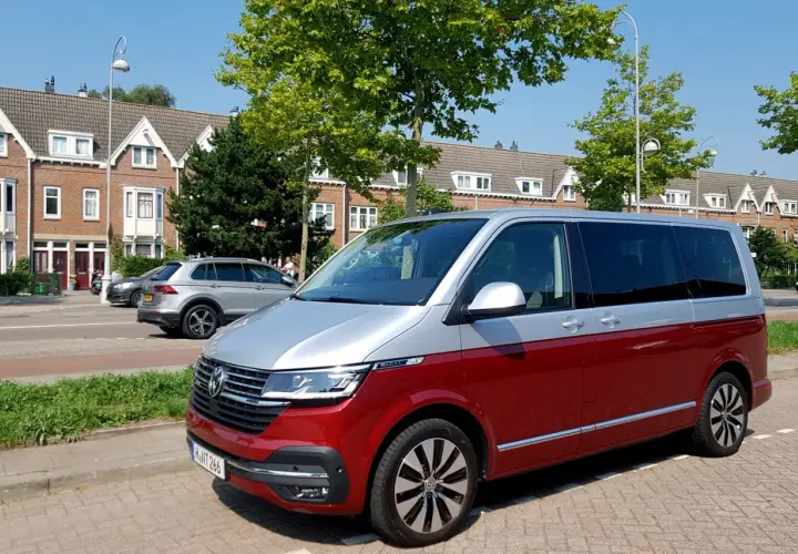 Dwukolorowy volkswagen van, czerwono-srebrny, zaparkowany na tle domów i drzew.
