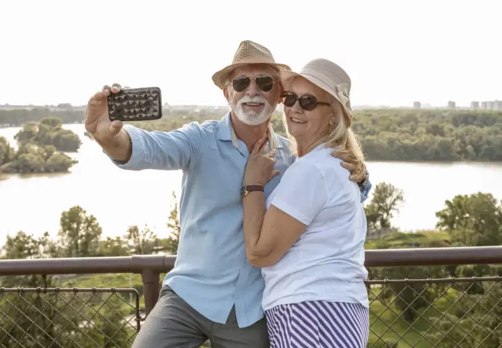 Uśmiechnięta para seniorów robi selfie na tle rzeki. Idealne wycieczki dla seniorów samolotem to świetny sposób na podróżowanie.