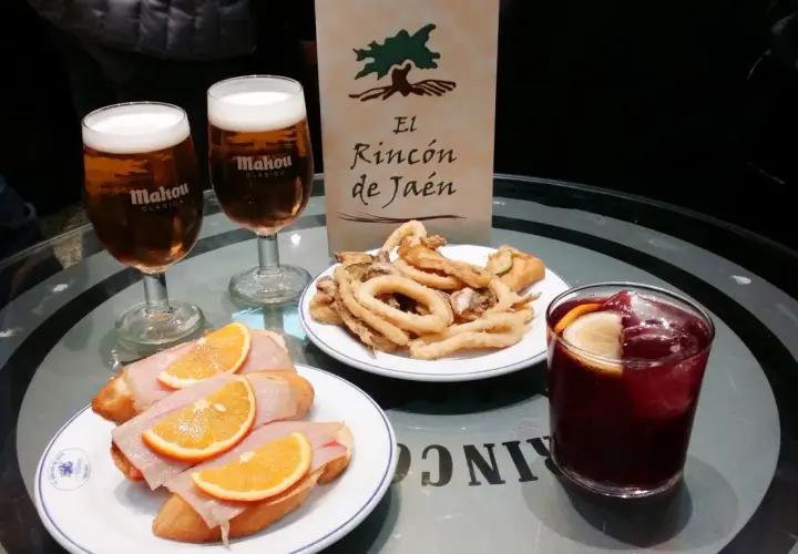 Dwa piwa Mahou, tapas z szynką i pomarańczą, smażone kalmary i sangria na stole w El Rincón de Jaén.