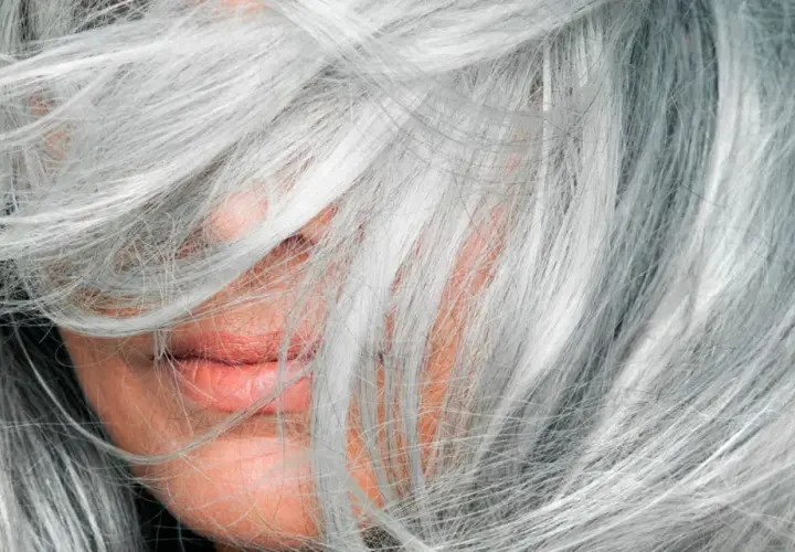 Mechas en pelo blanco natural, cubriendo parte del rostro y labios.