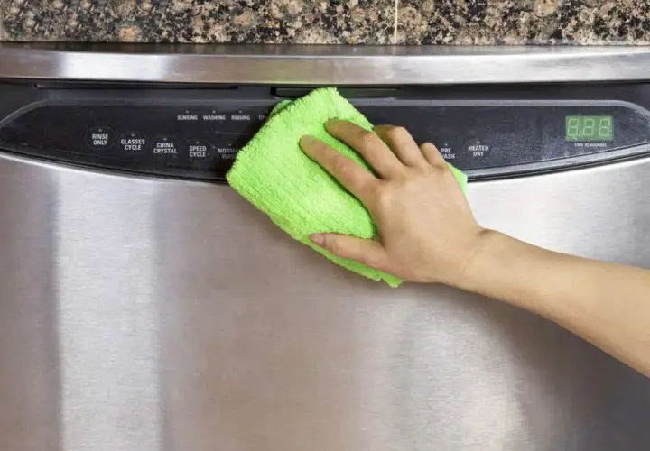 Mano limpiando un lavavajillas de acero inoxidable con un paño verde. Aprende como limpiar el acero inoxidable para mantenerlo brillante.