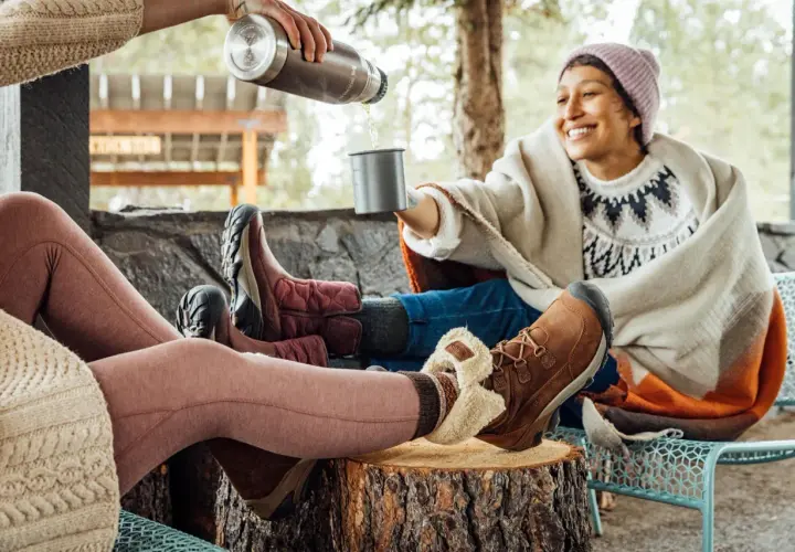 Cozy friends share drinks outdoors, their feet snug in warm shoes to keep feet warm.