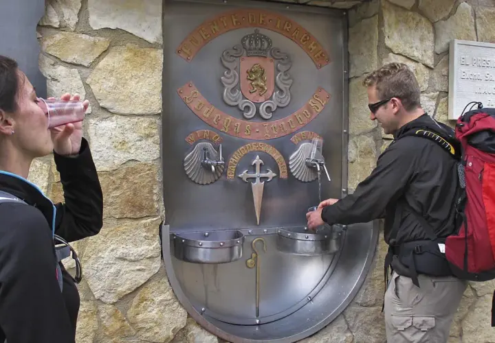 Peregrinos en el Camino de Santiago se refrescan en la fuente del vino y agua de Irache.