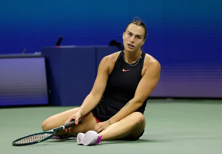 Zmęczona tenisistka siedzi na korcie, trzymając rakietę. Intensywny mecz tenis kobiet.