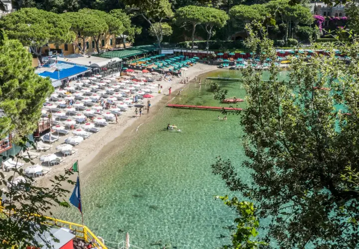 Plage animée d'une ville de la Riviera italienne, avec des parasols blancs, des chaises longues et des baigneurs dans l'eau cristalline.