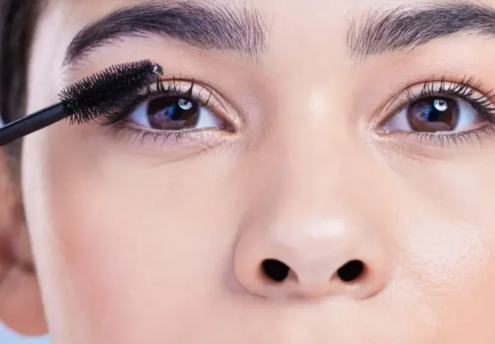 Eine Hand trägt Mascara auf die Wimpern auf, um runde Augen zu schminken.