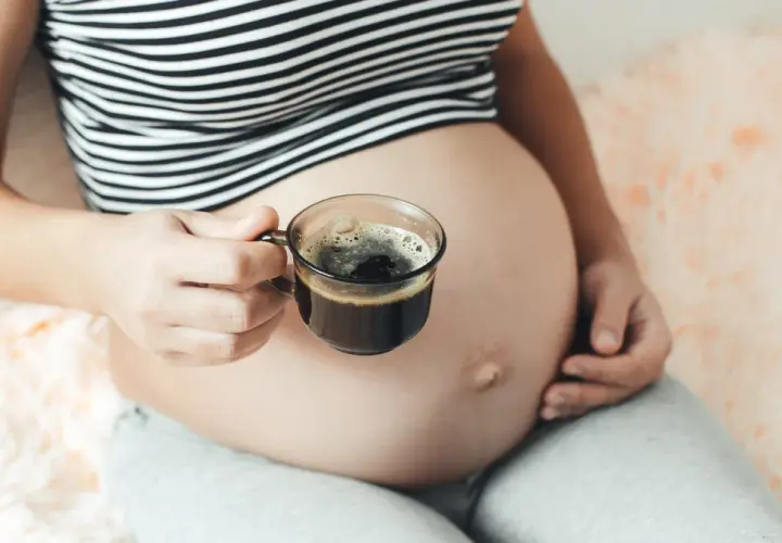 Kobieta w ciąży trzyma filiżankę kawy. Delikatny napój dla przyszłych mam.