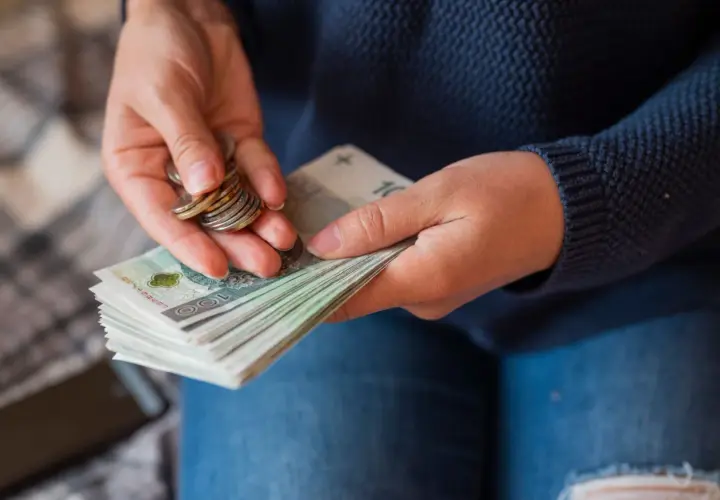 Dłonie liczą banknoty i monety, przygotowując się do wypłaty pensji.