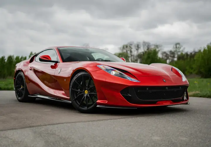 Czerwone, ładne auta sportowe Ferrari na tle zieleni i chmur.