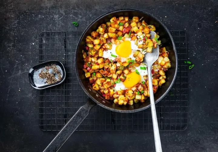 Poêle de pomme de terre oeuf, un plat réconfortant avec des dés de pommes de terre dorés et deux œufs au plat, garni de ciboule.