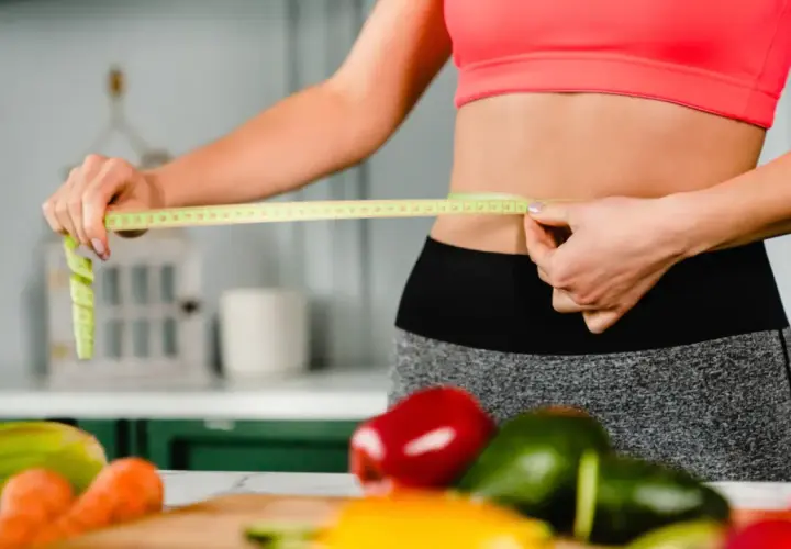 Mujer mide su cintura con cinta métrica, rodeada de verduras frescas. ¿La menopausia adelgaza o engorda?