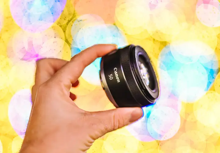 Dłoń trzyma obiektyw Canon 50mm na tle kolorowych świateł bokeh.