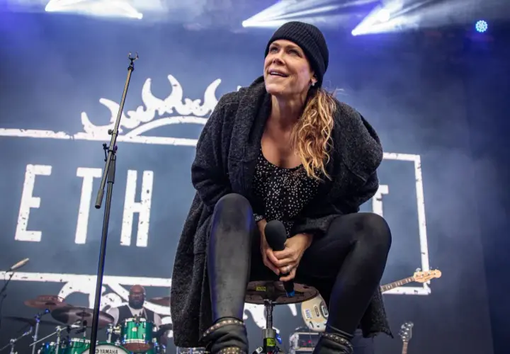 Beth Hart na scenie, w czapce i swetrze, śpiewa swoje utwory. W tle logo z koroną i perkusista.
