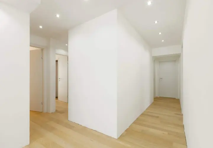 Un corridoio moderno con pavimenti in legno chiaro e una parete in cartongesso curvo che crea un effetto dinamico.