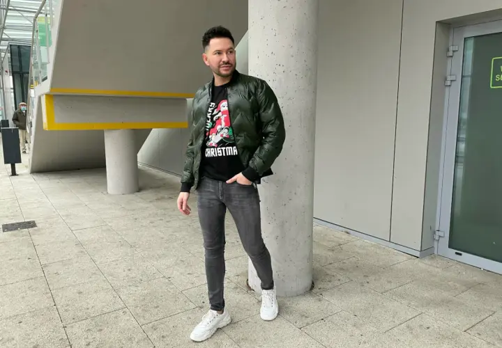 Mężczyzna w zielonej bomberce i szarych jeansach, zastanawia się, jakie buty do bomberki będą najlepsze. Postawił na białe sneakersy.