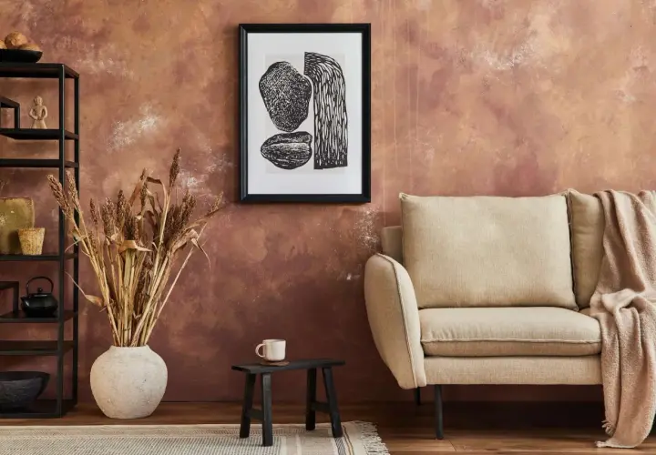 Rusty, textured wall – świetny pomysł co na ścianę zamiast farby. Obok kanapa, grafika i suszone trawy.