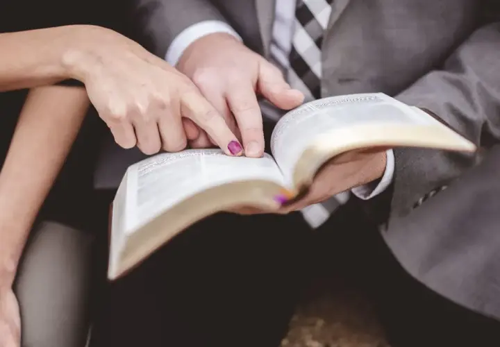 Dłonie pary wskazują na tekst w Biblii, symbolizując wspólną drogę i ewangelia na ślub.