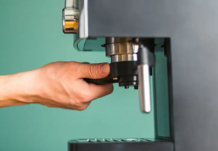 Dłoń przygotowuje ekspres do zaparzenia podwójnego espresso, czyli **doppio kawa**.