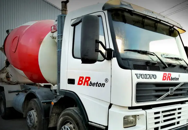 Biała ciężarówka Volvo z czerwoną obrotową beczką na beton. To jeden z rodzajów betoniarek, gotowy do transportu budowlanego.