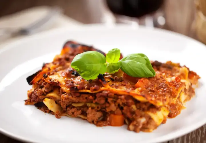 Une part de lasagnes à la bolognaise, garnie de basilic frais. Un plat réconfortant, parfait avec un verre de vin rouge. Quel vin avec des lasagnes ?