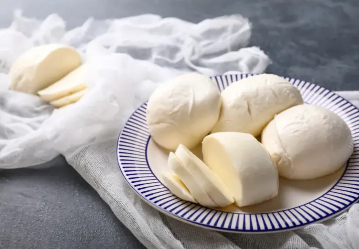 Świeża mozzarella na talerzu, pokrojona i w całości. Czy mozzarella podnosi cukier? Ten ser jest niskowęglowodanowy.