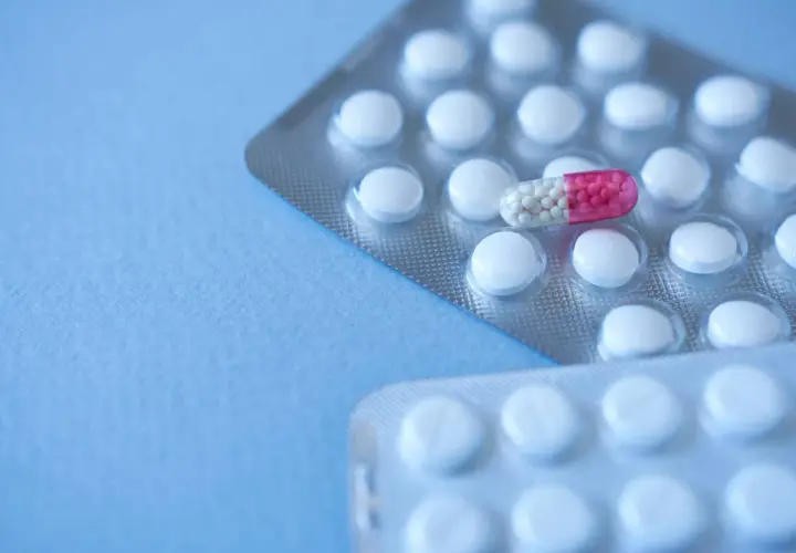 Dwie blistry białych tabletek, jedna z nich zawiera kapsułkę z różowymi granulkami, przypominającą clonazepam.