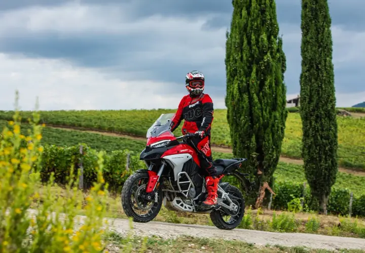 Un motociclista in tuta rossa sfreccia tra i vigneti toscani, godendosi le strade più belle della Toscana in moto.