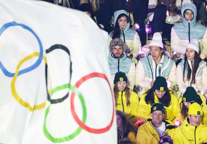Młodzi sportowcy w barwach narodowych, z flagą olimpijską w tle, czekają na start reprezentacji Polski na Zimowe Igrzyska Olimpijskie 2026.