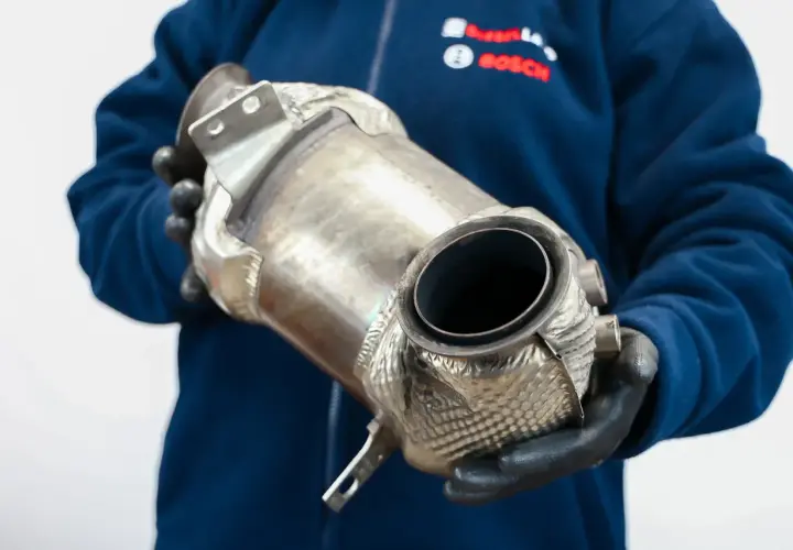 Mechanik w rękawiczkach trzyma element układu wydechowego, pokazując jak dbać o dpf.