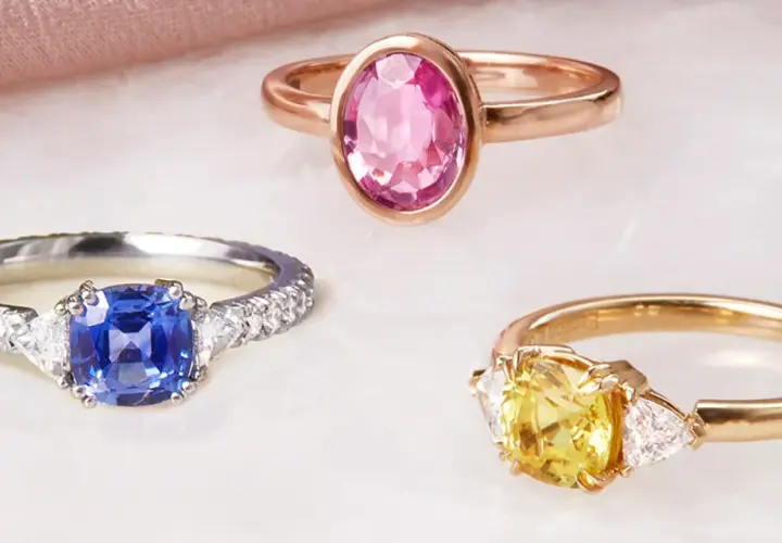 Drei Ringe mit Edelsteinen: ein blauer Saphir, ein gelber Saphir und ein rosa Saphir. Die Bedeutung von rosa Saphir steht für Liebe und Mitgefühl.