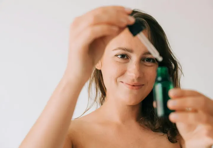 Kobieta z piegami trzymająca pipetkę z zieloną buteleczką.