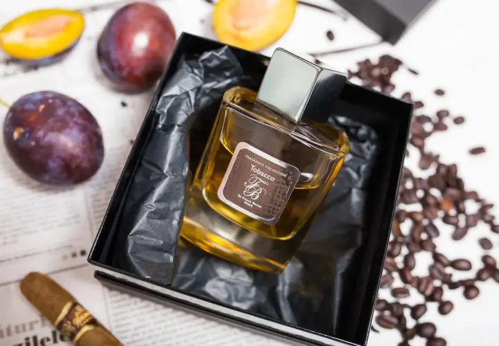 Perfumy "Tobacco" by Franck Boclet w eleganckim flakonie, otoczone śliwkami, kawą i cygarem.