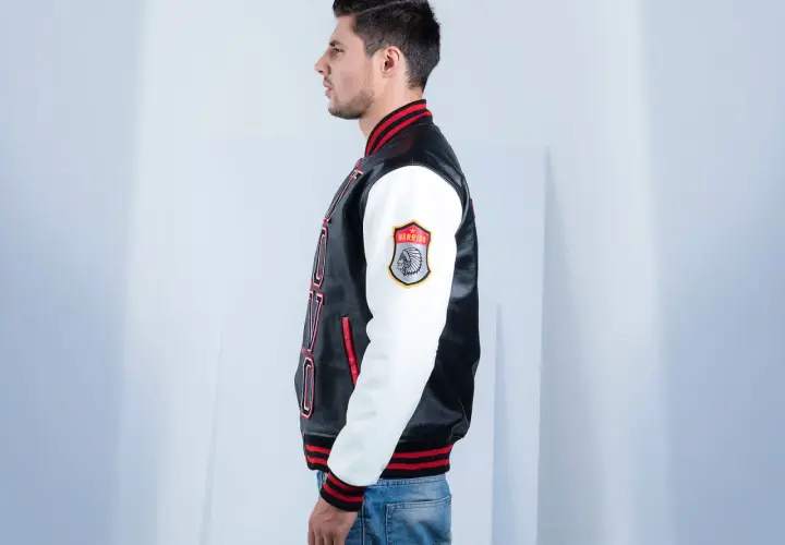 Man in profile wearing a black and white letterman jacket with red trim and a "Warrior" patch.