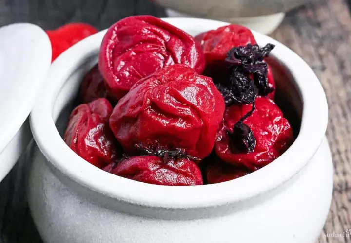 A white ceramic bowl filled with glistening, deep red umeboshi plums, ready for a delicious umeboshi recipe.