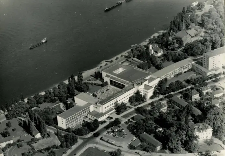 Luftaufnahme von Bonn am Rhein, als die Stadt Hauptstadt war. Mehrere Schiffe auf dem Wasser, Regierungsgebäude und Bäume.