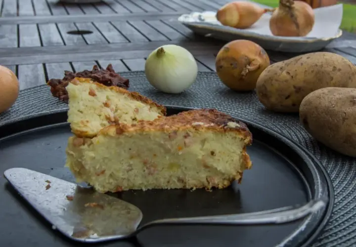 Babka ziemniaczana przepis babci: złocista, pachnąca babka ziemniaczana z boczkiem, obok surowe ziemniaki, cebula i jajko.
