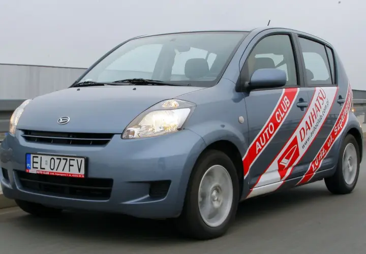 Szary Daihatsu Sirion z napisem "AUTO CLUB DAIHATSU" na boku, jadący po drodze.