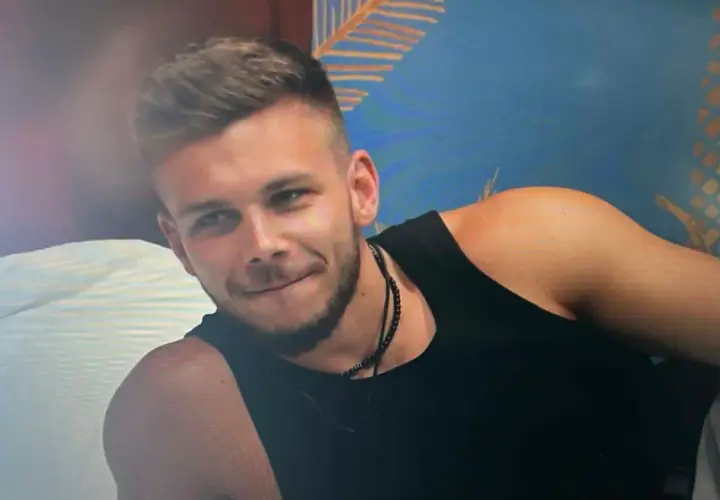 Bartek z Hotel Paradise, z uśmiechem na twarzy, w czarnej koszulce, na tle tropikalnej tapety.
