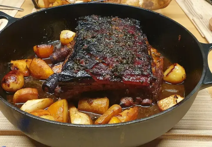 Poitrine de porc au four cuisson lente, dorée et savoureuse, accompagnée de pommes de terre rôties dans un plat en fonte.